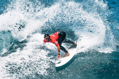 Surfer in a red shirt and black wetsuit riding a wave on a clear day.