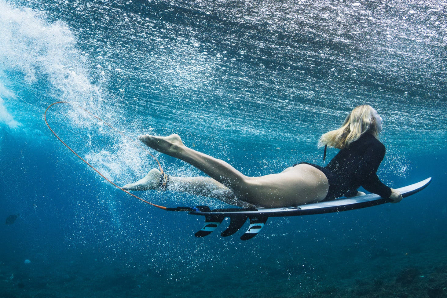Person lying on a surfboard underwater with a wave in the background