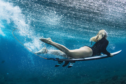 Person lying on a surfboard underwater with a wave in the background